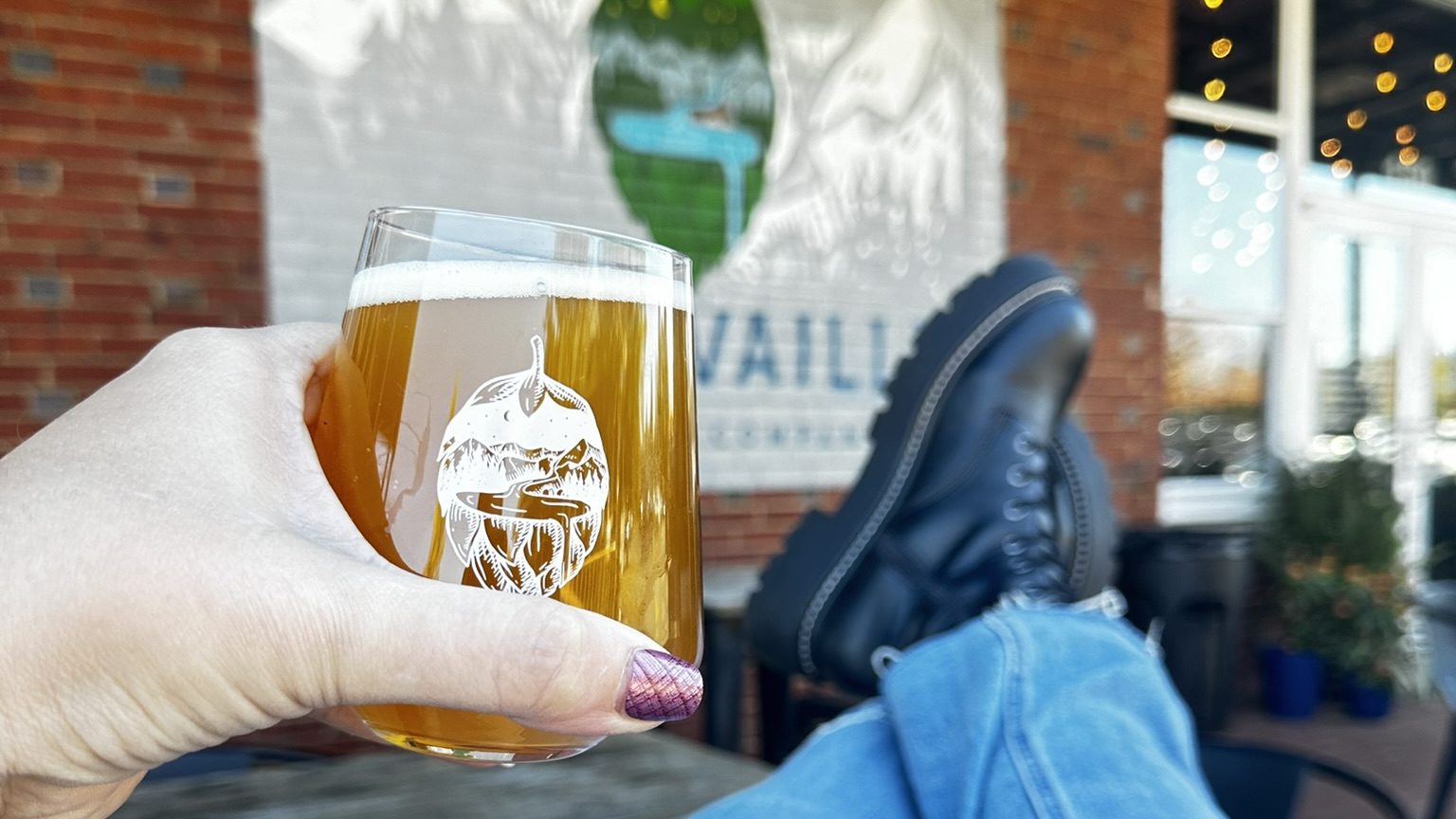 Boots on a table while holding a rastal full of beer while toasting a mural that says "Trouvaille".